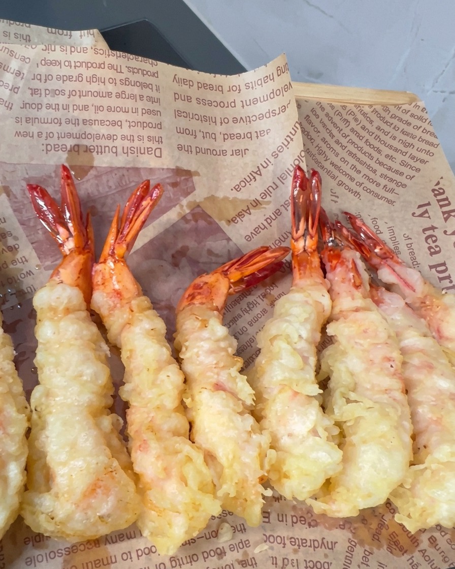 Gamberi impastellati che friggono in olio caldo con punte croccanti che si formano in superficie.