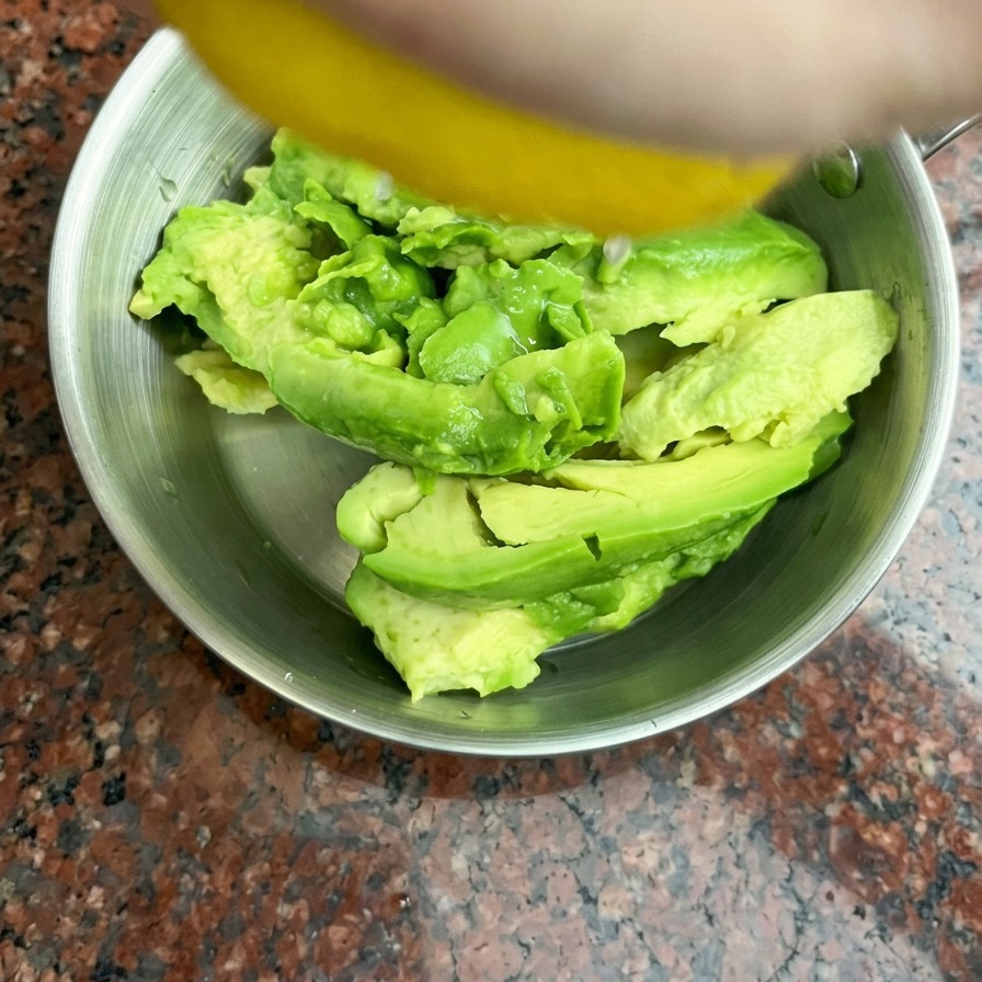Succo di limone fresco spremuto a mano su metà avocado allinterno di una ciotola in acciaio inossidabile.