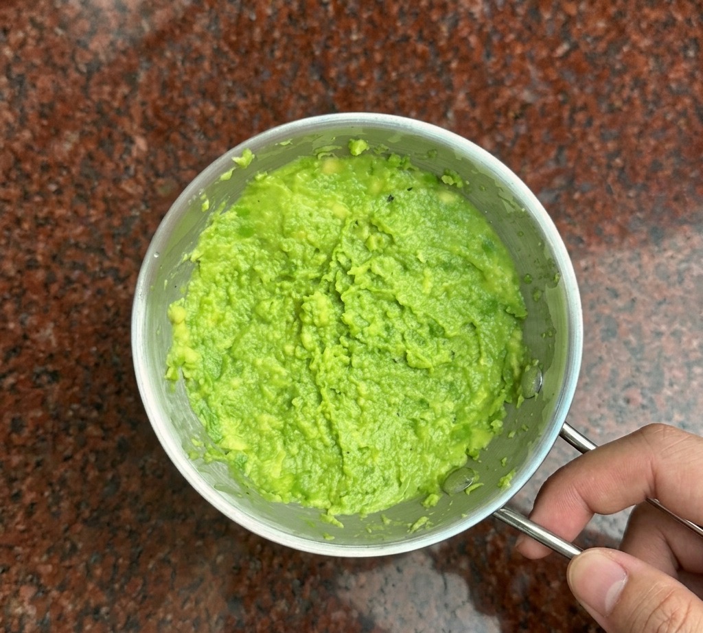 Una forchetta di metallo schiaccia lavocado verde brillante in una purea densa dentro una ciotolina.
