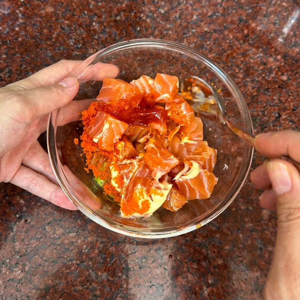Una mano mescola delicatamente i cubetti di salmone e la salsa cremosa arancione con un cucchiaio.