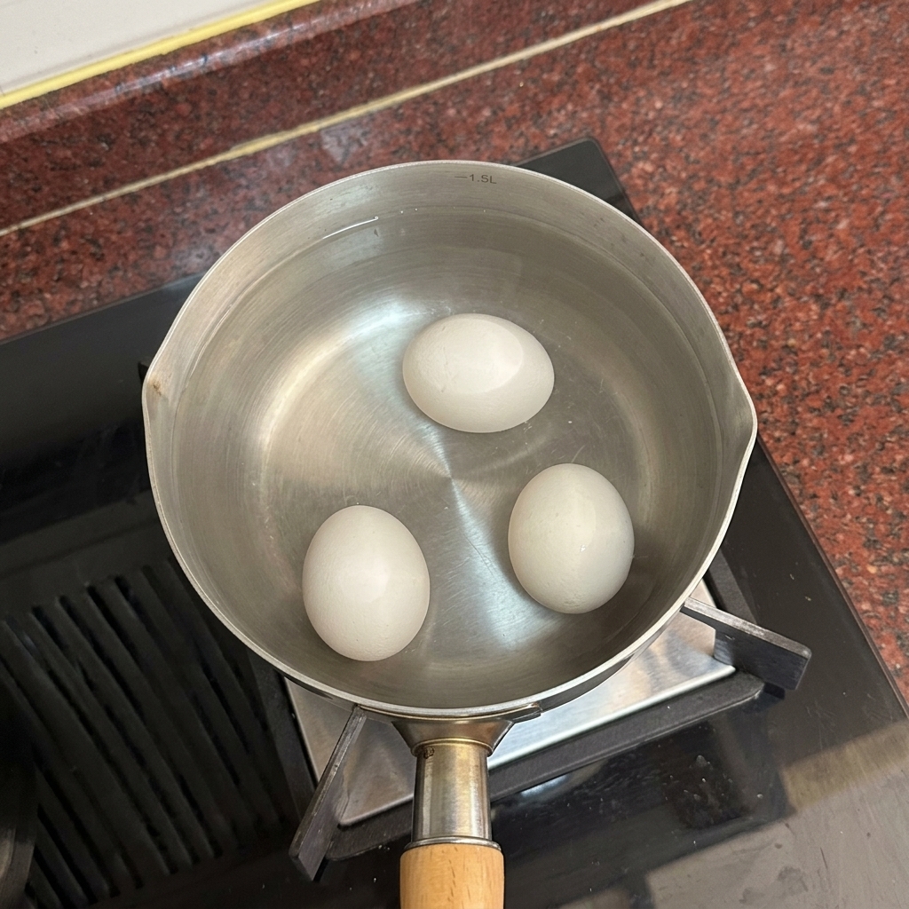 Tre uova bianche adagiate sul fondo di una pentola piena di acqua calda e limpida.