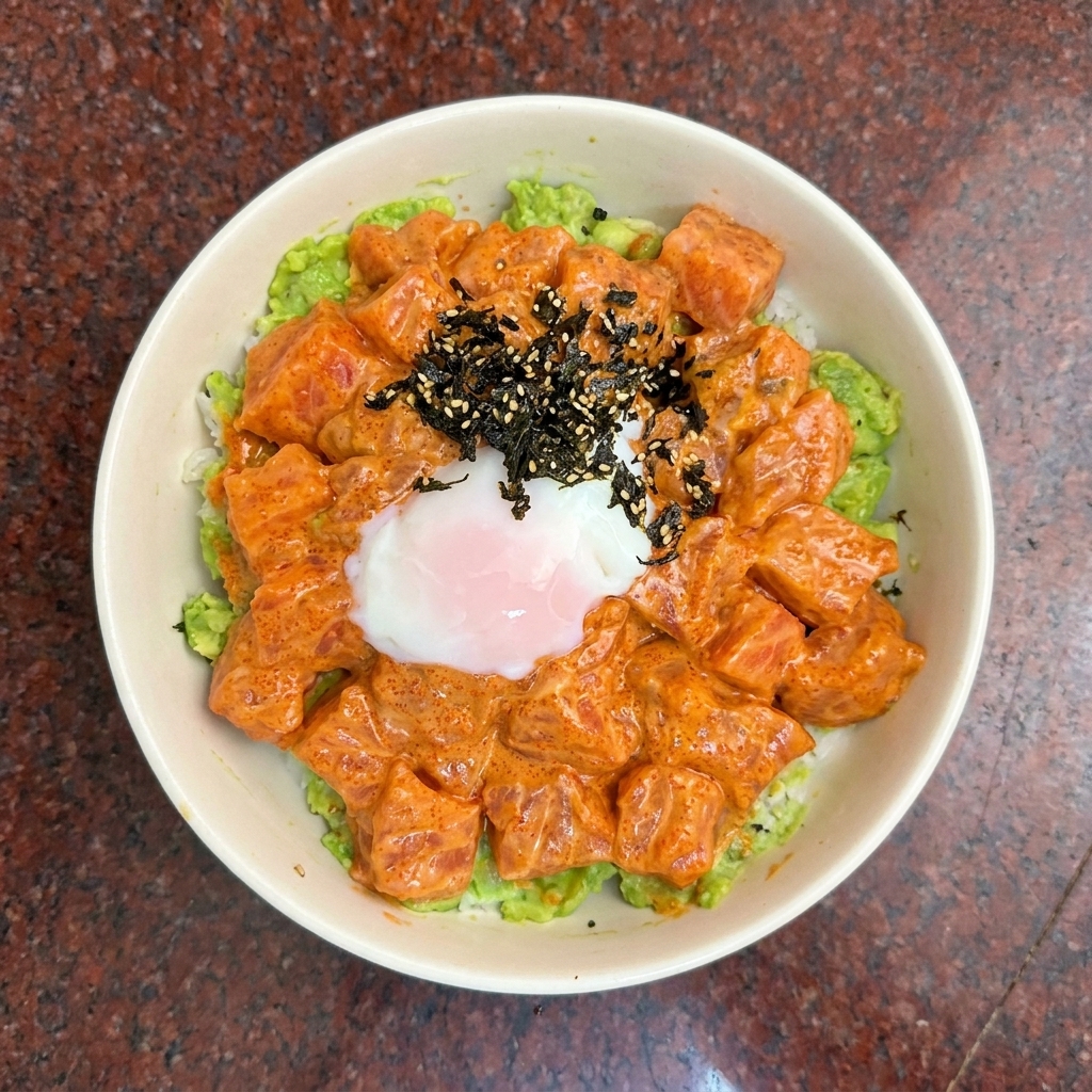 Vista dallalto di una poke bowl di salmone guarnita con un uovo morbido e condimento di alga scura.