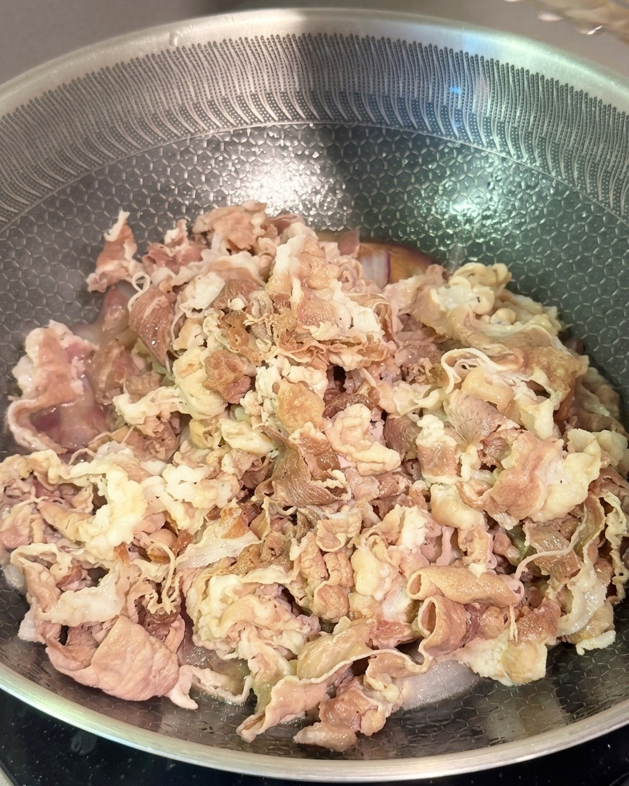 Teneri straccetti di manzo sbollentati che vengono saltati con cipolle rosse e una salsa scura in un wok dacciaio.