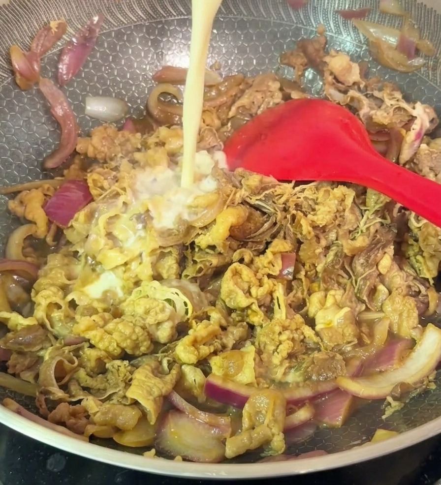 Un filo di miscela chiara di amido che viene versato in un wok con manzo saltato e cipolle rosse.