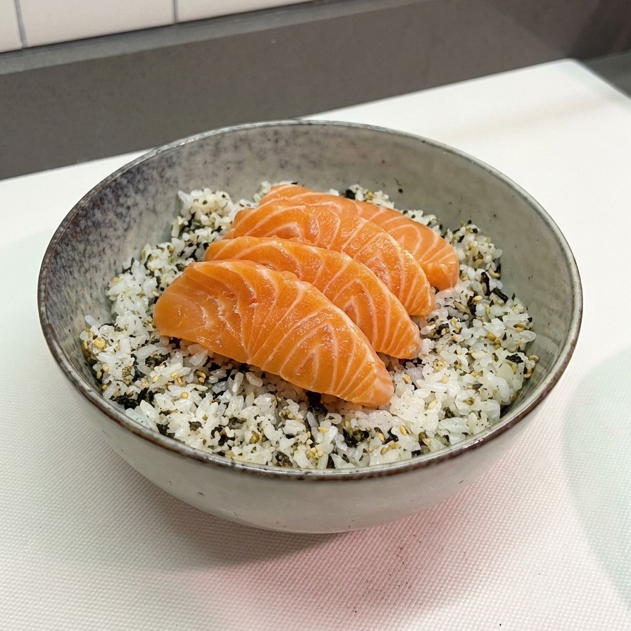 Quattro fette spesse di salmone dallarancione vivo disposte ordinatamente su un letto di riso bianco con scaglie di alga nori in una ciotola di ceramica grigia.
