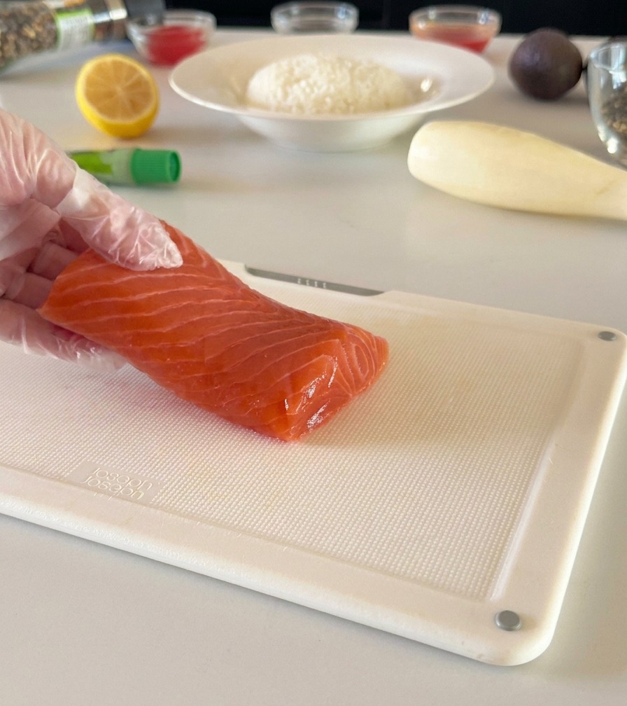 Un filetto di salmone fresco appoggiato su un tagliere bianco mentre viene tagliato a cubetti.