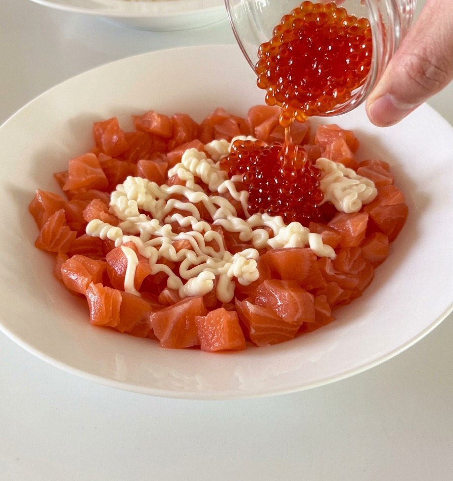 Cubetti di salmone fresco in una ciotola bianca conditi con uova di pesce rosso e maionese.
