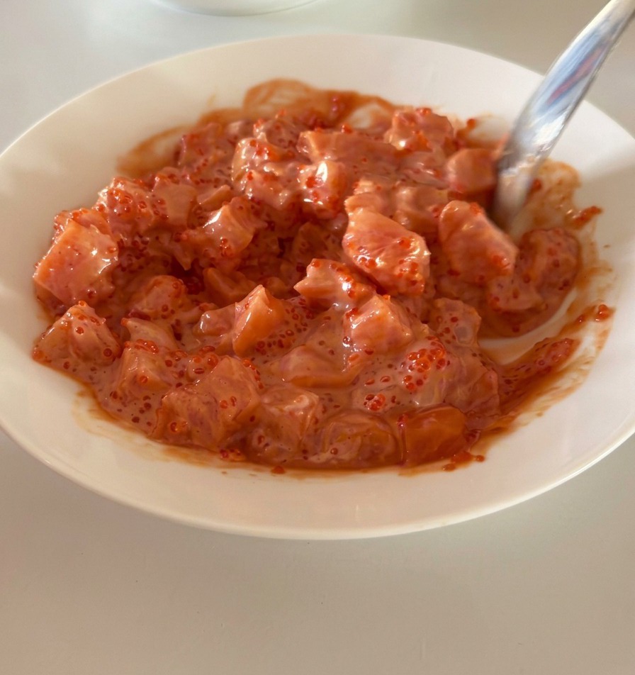 Una ciotola bianca con cubetti di salmone conditi riposta sul ripiano di un frigorifero.