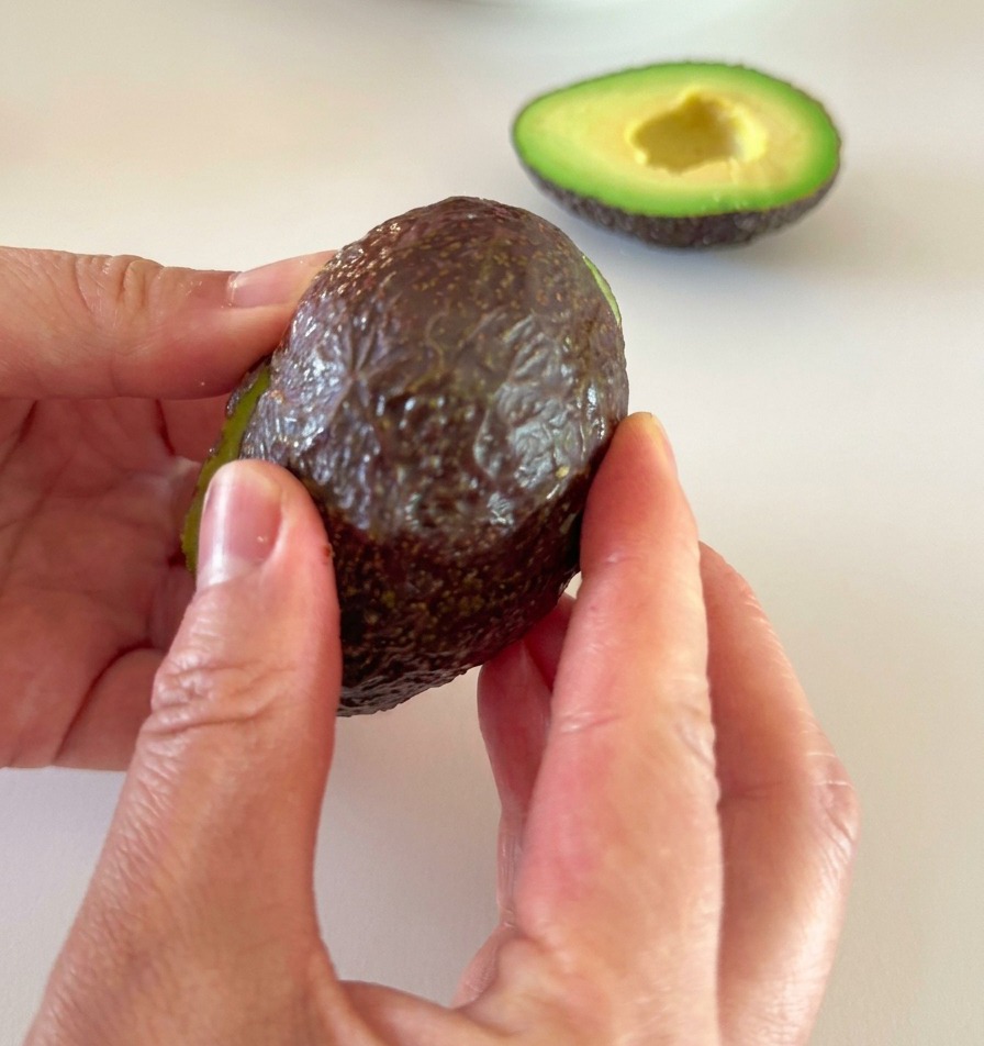 Mani che rimuovono delicatamente la buccia scura da metà avocado maturo.