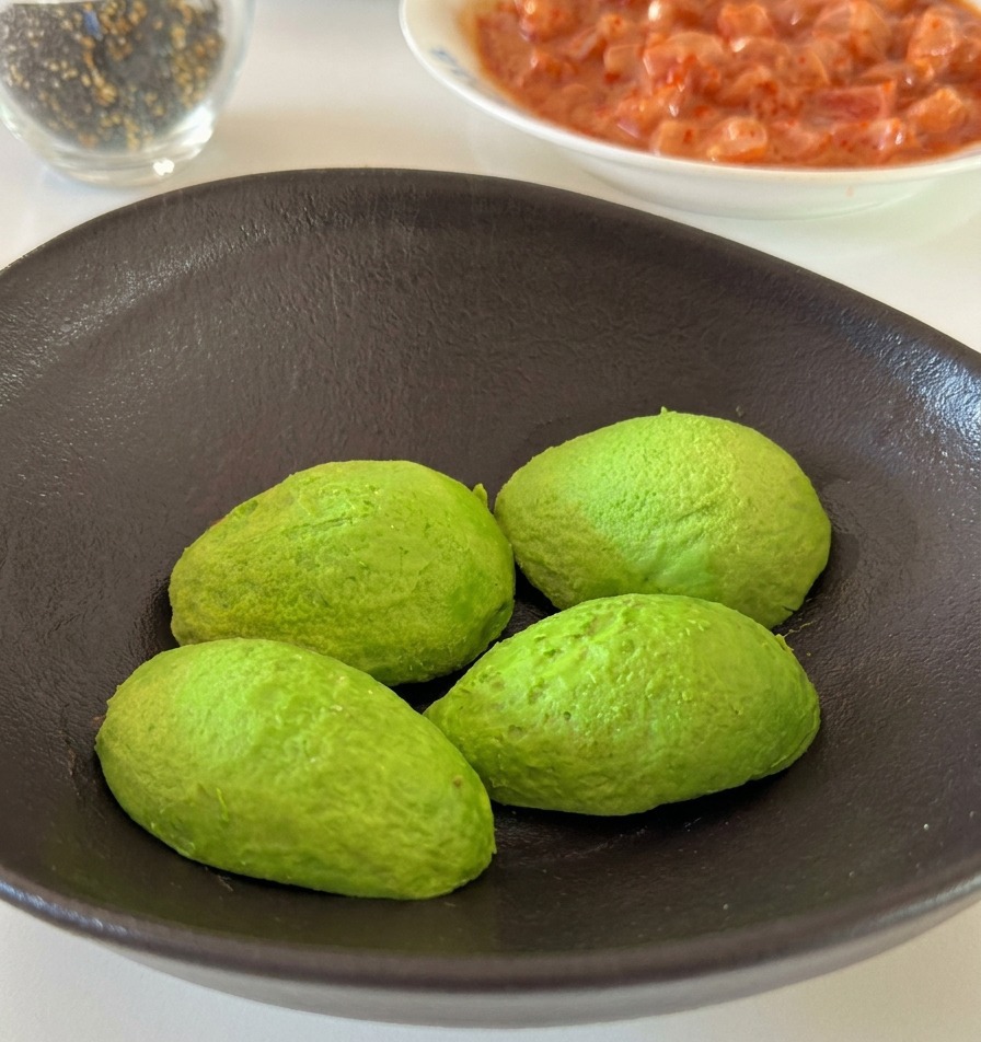 Una mano che spreca uno spicchio di limone sopra le metà di un avocado in una ciotola.