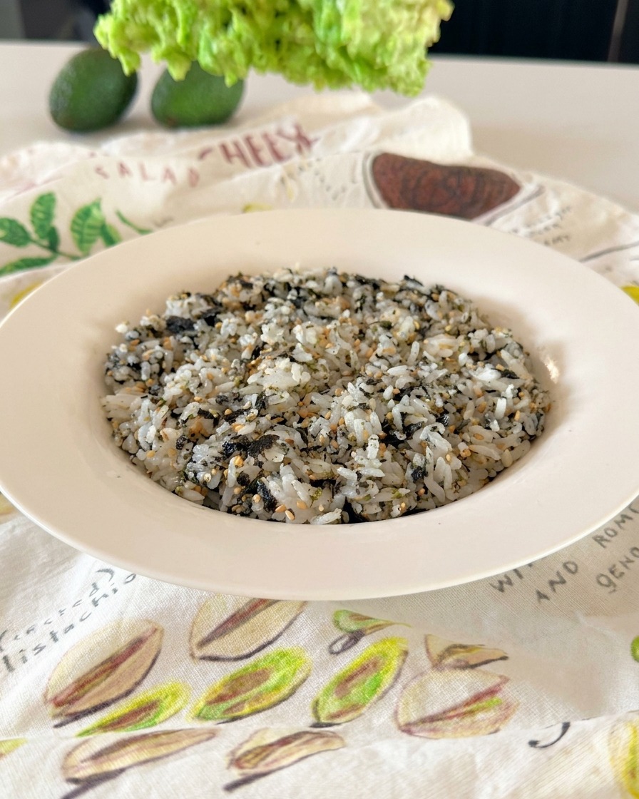 Una ciotola con riso ricoperto da semi di sesamo e fiocchi di alga nori verde scuro.
