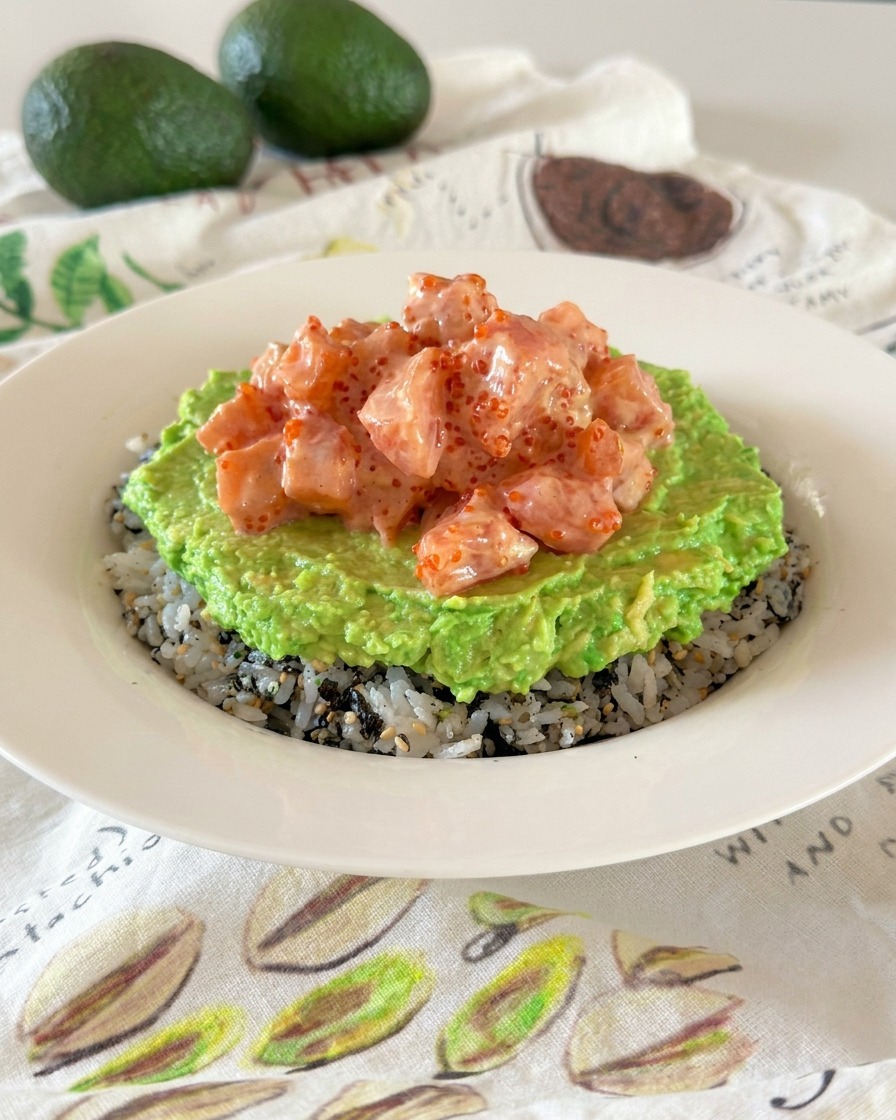 Una poke bowl che mostra i diversi strati di riso condito, crema di avocado e cubetti di salmone cremoso.
