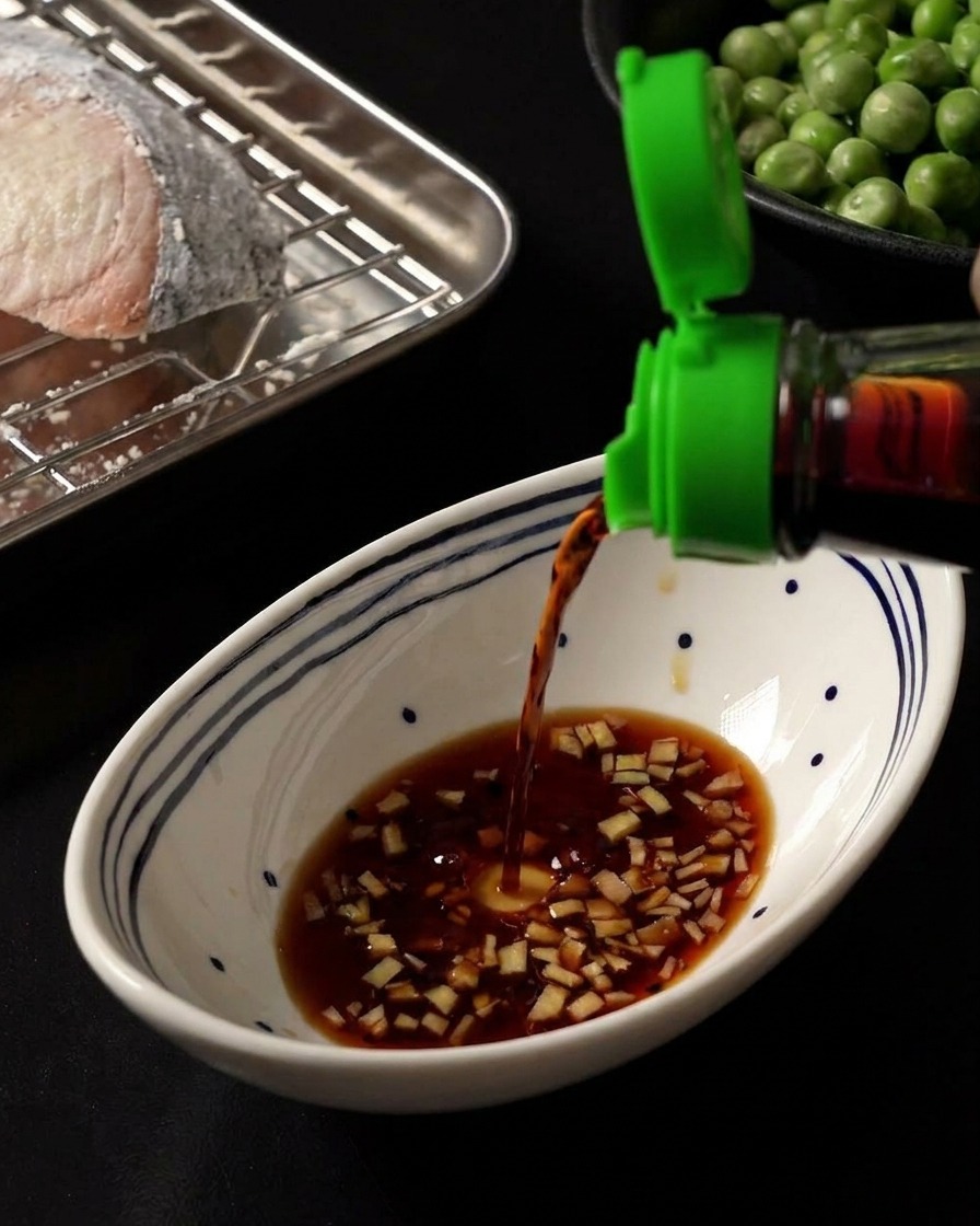 Salsa di soia scura versata in una ciotola bianca che contiene una base di zenzero tritato e miele.