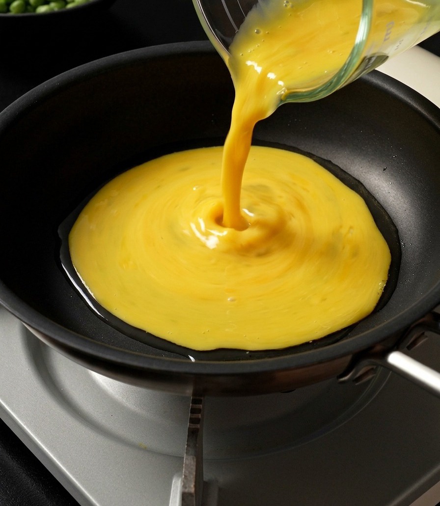 Miscela di uova sbattute gialle versata da un misurino di vetro in unampia padella per formare una sottile frittata.