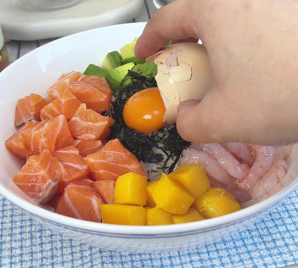 Un tuorlo duovo arancione che viene versato da un mezzo guscio duovo sulla guarnizione di alga nori nel mezzo della ciotola.