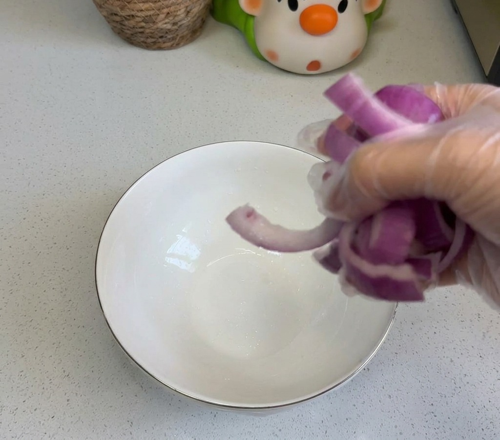 Una persona che versa cipolle rosse affettate in una ciotola di ceramica bianca sul bancone della cucina.