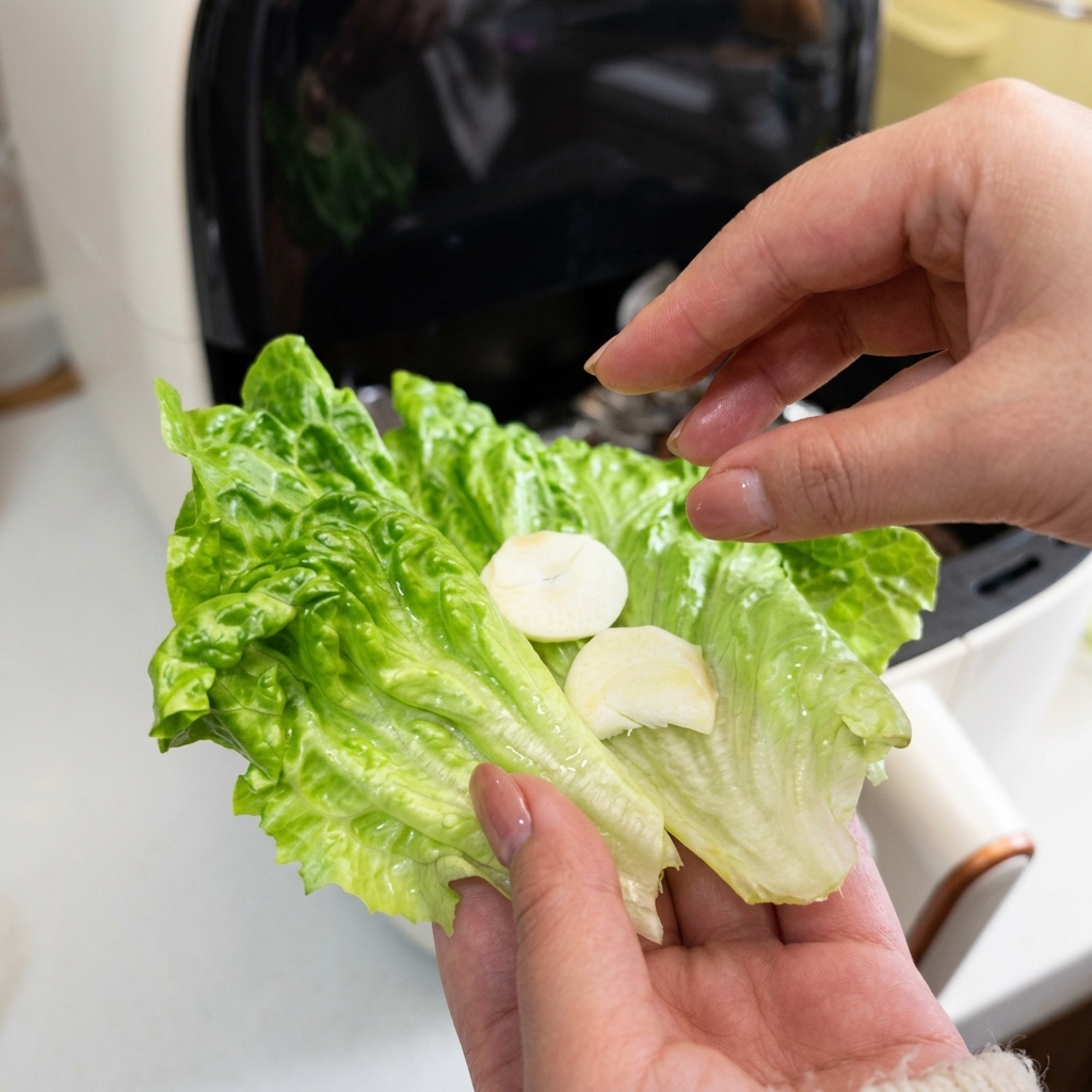Primo piano di una mano che tiene una foglia di lattuga verde condita con due fette di aglio fresco bianco.