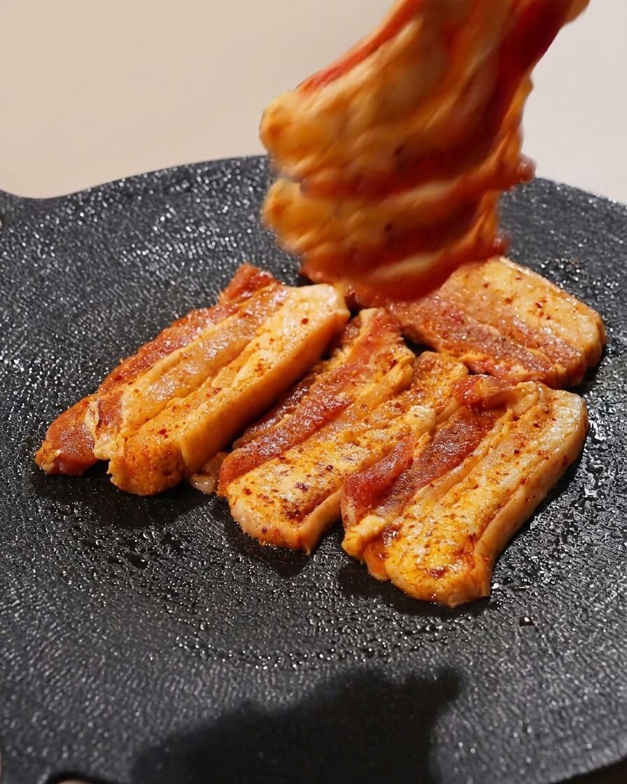 Diverse fette di pancetta di maiale disposte su una piastra calda.