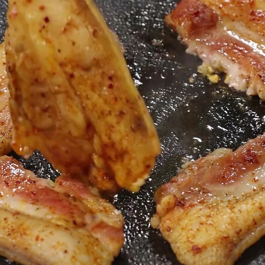Pinze da cucina in metallo che girano una fetta di pancetta dorata sulla piastra sfrigolante.