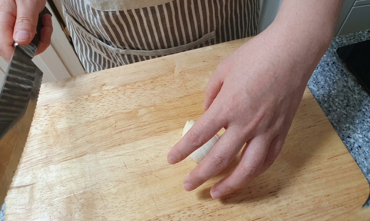Un coltello utilizzato per tagliare a fette sottili e verticali una cipolla bianca su una superficie di legno.