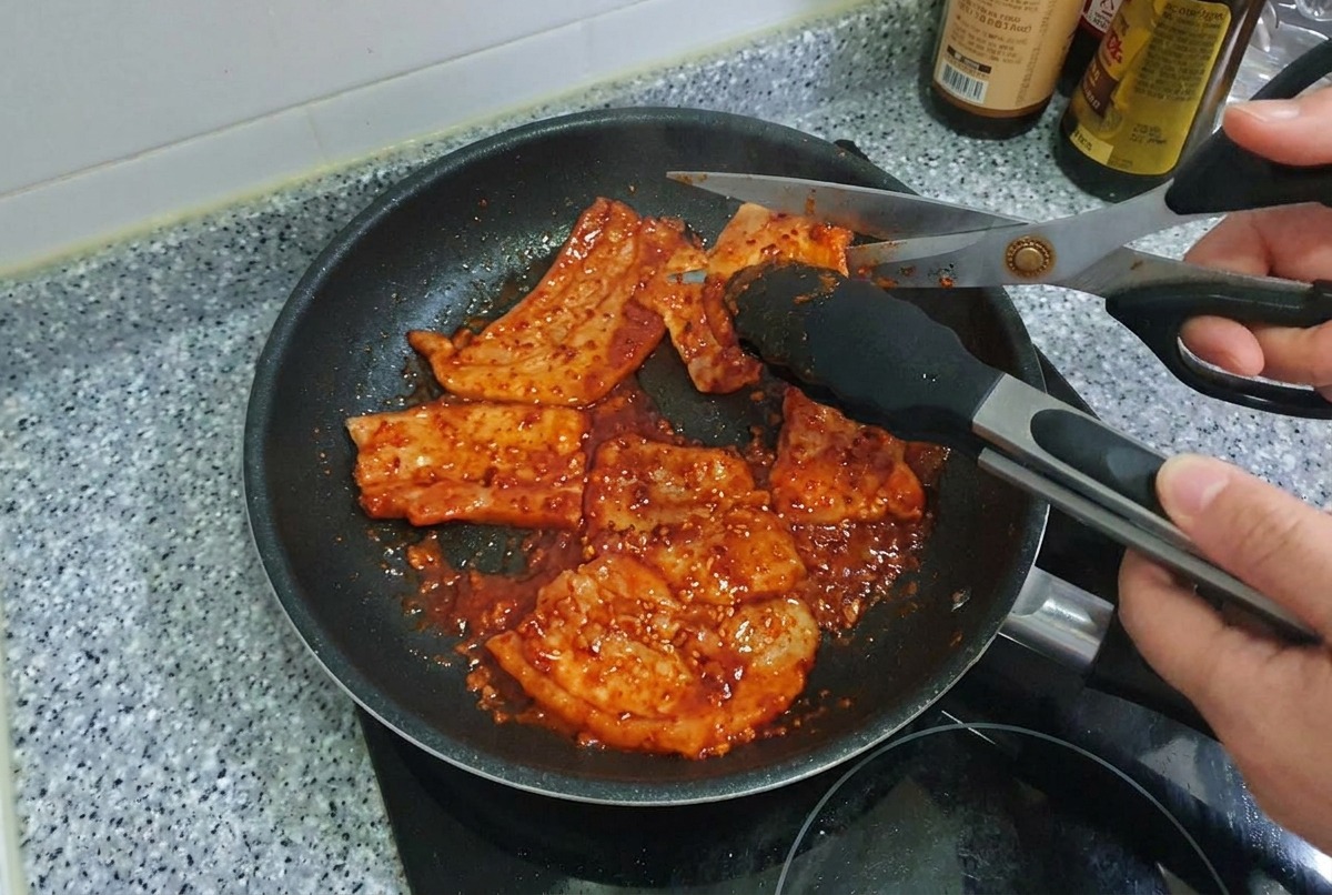 Forbici da cucina che tagliano strisce di pancetta di maiale grigliata e piccante allinterno di una padella.
