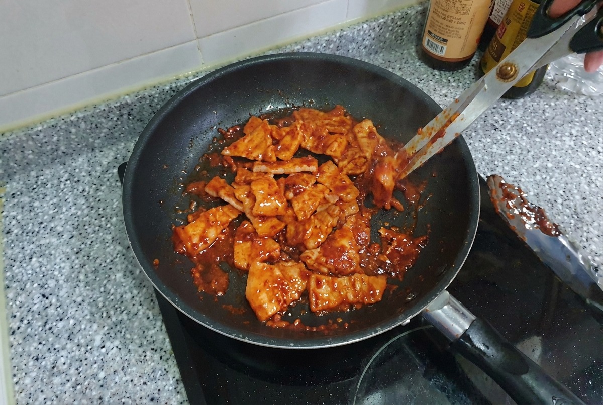 Pezzetti di pancetta di maiale piccante che vengono saltati in padella, apparendo lucidi e caramellati.