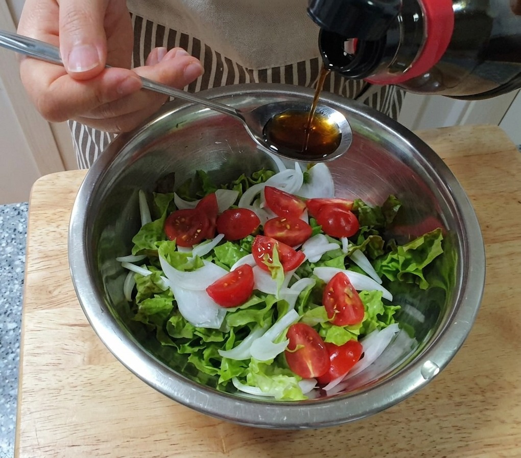 Il condimento che viene versato con un cucchiaio su una ciotola di lattuga, cipolle e pomodorini.