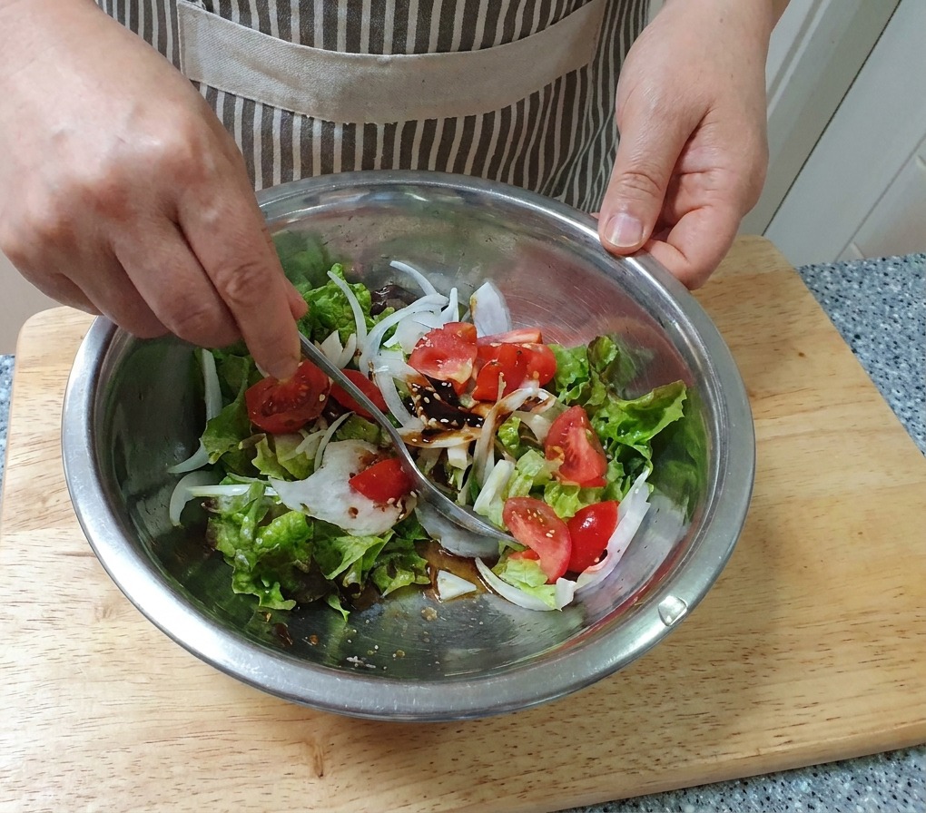 Una mano che mescola uninsalata di verdure fresche con un cucchiaio in una grande ciotola di acciaio inossidabile.