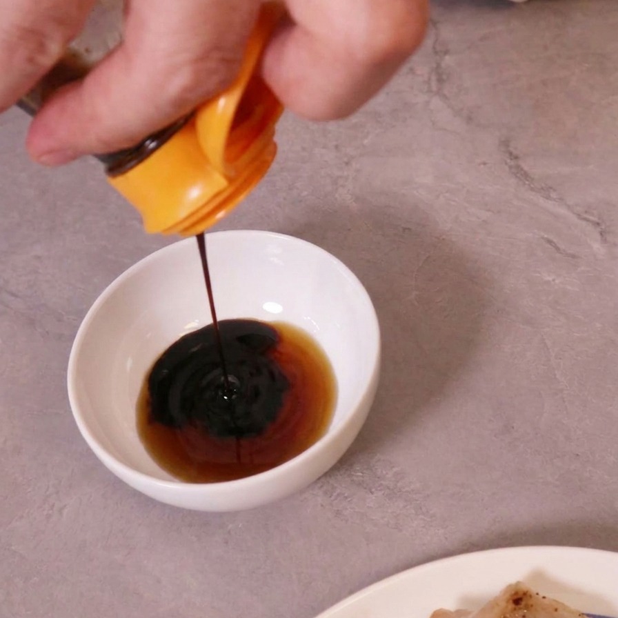 Salsa di soia scura versata in una ciotola bianca contenente un liquido più chiaro per preparare una salsa di accompagnamento.