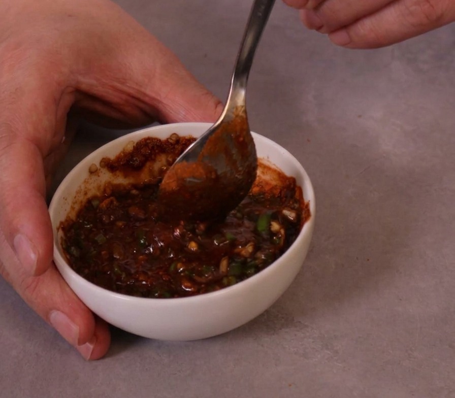 Una densa salsa piccante di colore rosso vivo mescolata con un cucchiaio di metallo in una piccola ciotola di ceramica.