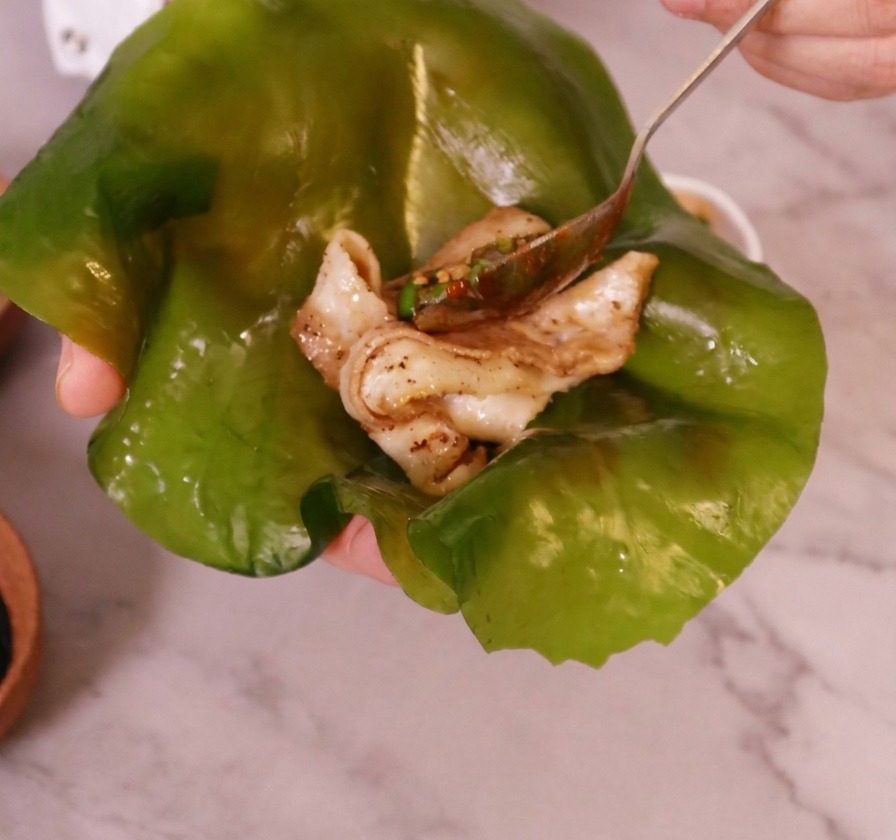 Una mano che tiene una grande foglia di alga kelp traslucida con un pezzo di pancetta cotta posizionato al centro.