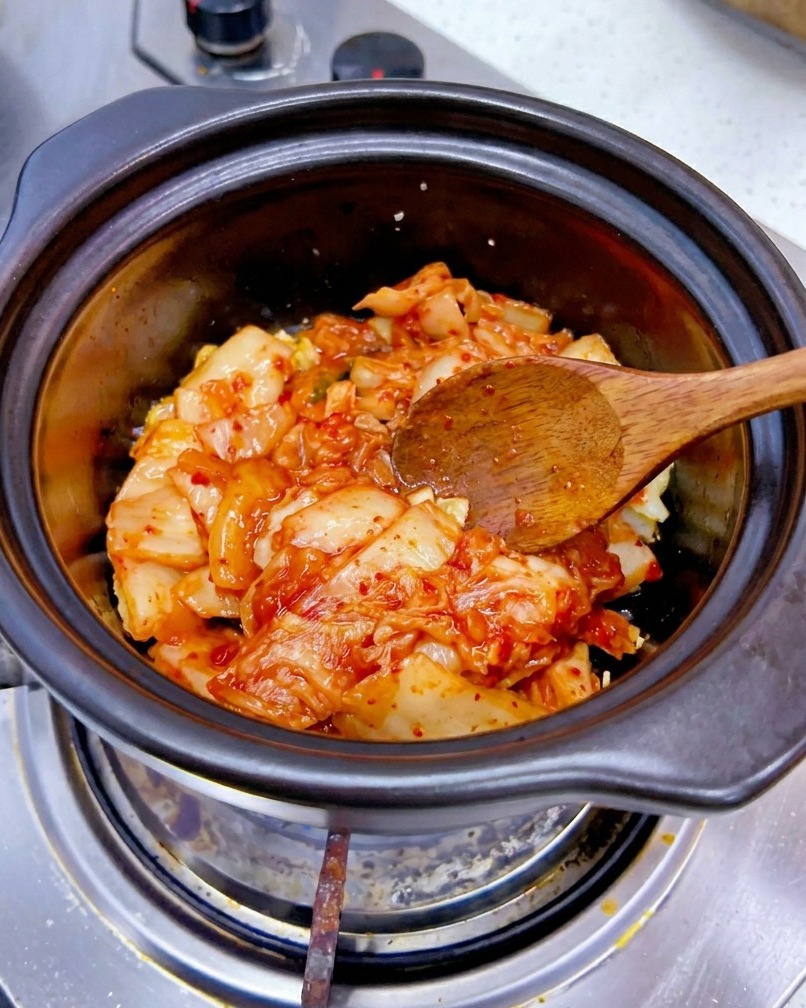 Una porzione di kimchi di cavolo rosso tritato viene aggiunta in una pentola con laglio soffritto.