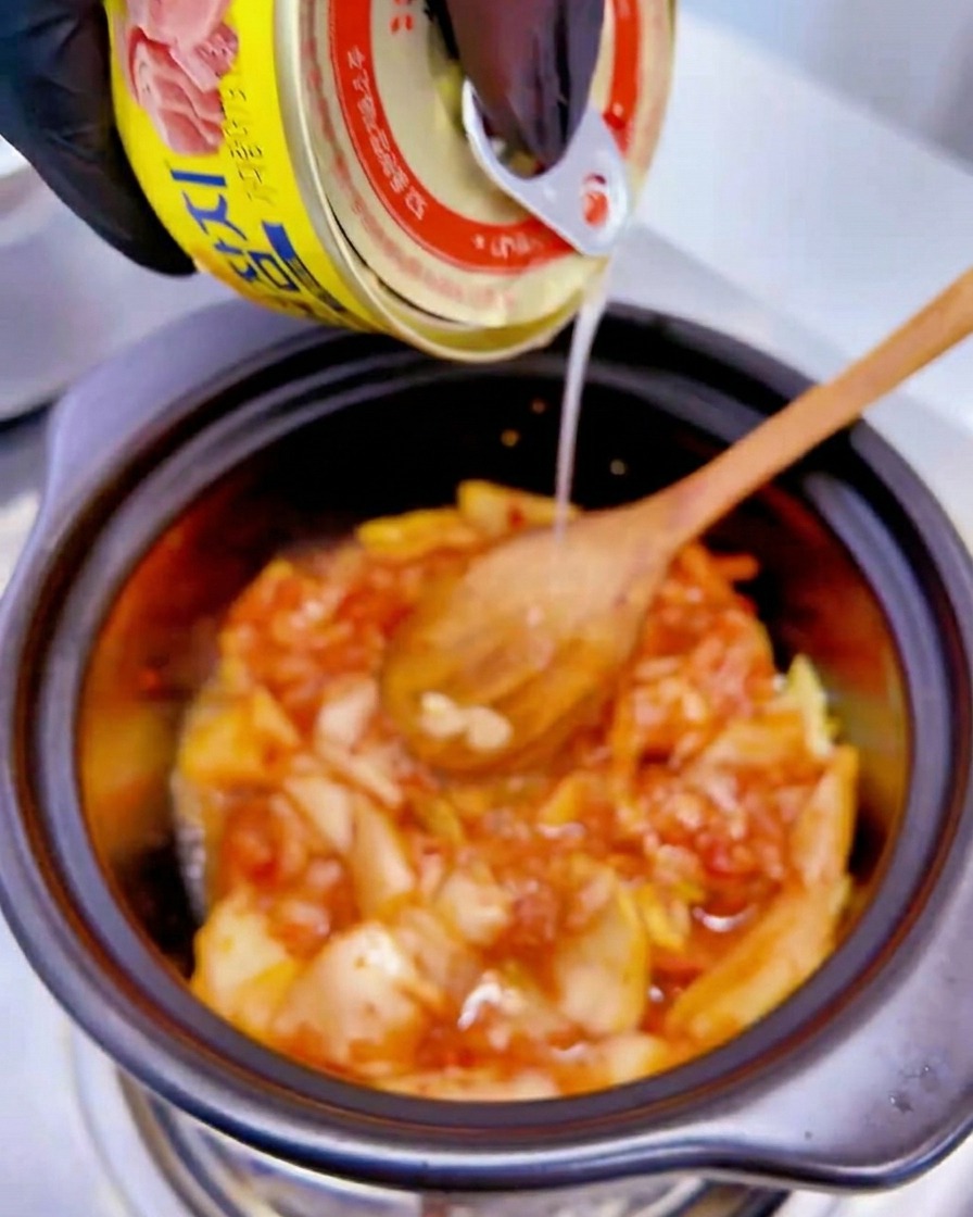 Il liquido da una lattina gialla di tonno viene versato sul composto di kimchi nella pentola.