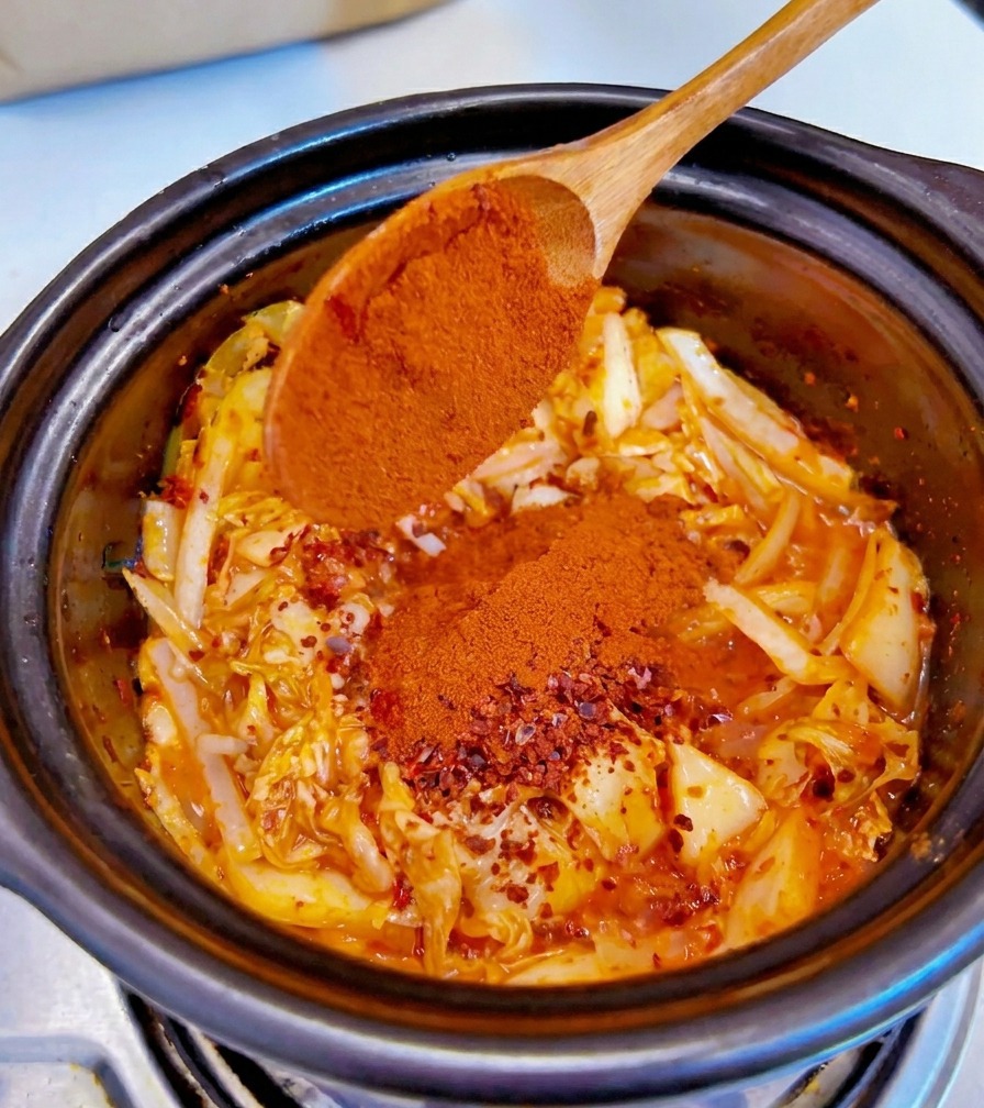 Peperoncino rosso in polvere fine viene aggiunto da un cucchiaio di legno sul composto di kimchi e cipolle.