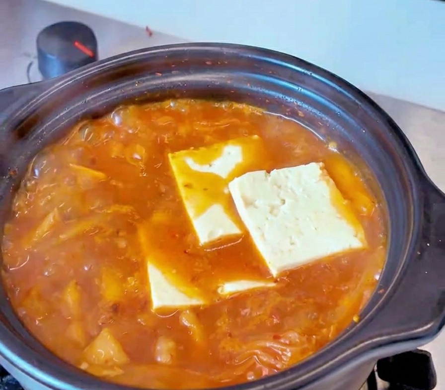 Fette rettangolari di tofu bianco adagiate nel brodo rosso e bollente dello stufato di kimchi.