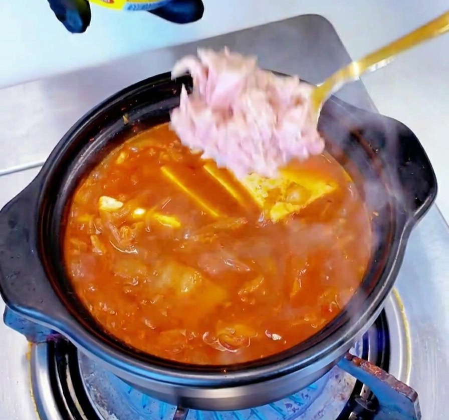 Pezzi di tonno chiaro in scatola vengono adagiati con un cucchiaio al centro di uno stufato rosso che sobbolle.