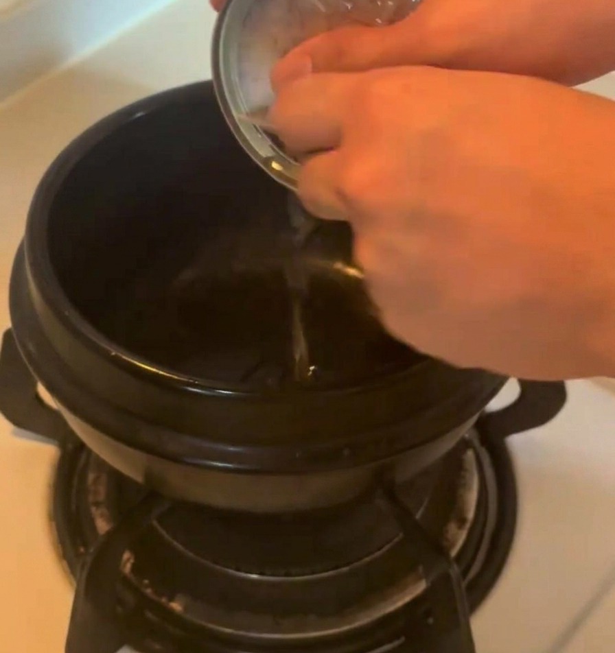 Olio saporito versato da una lattina metallica di tonno in una pentola di ceramica scura sui fornelli.