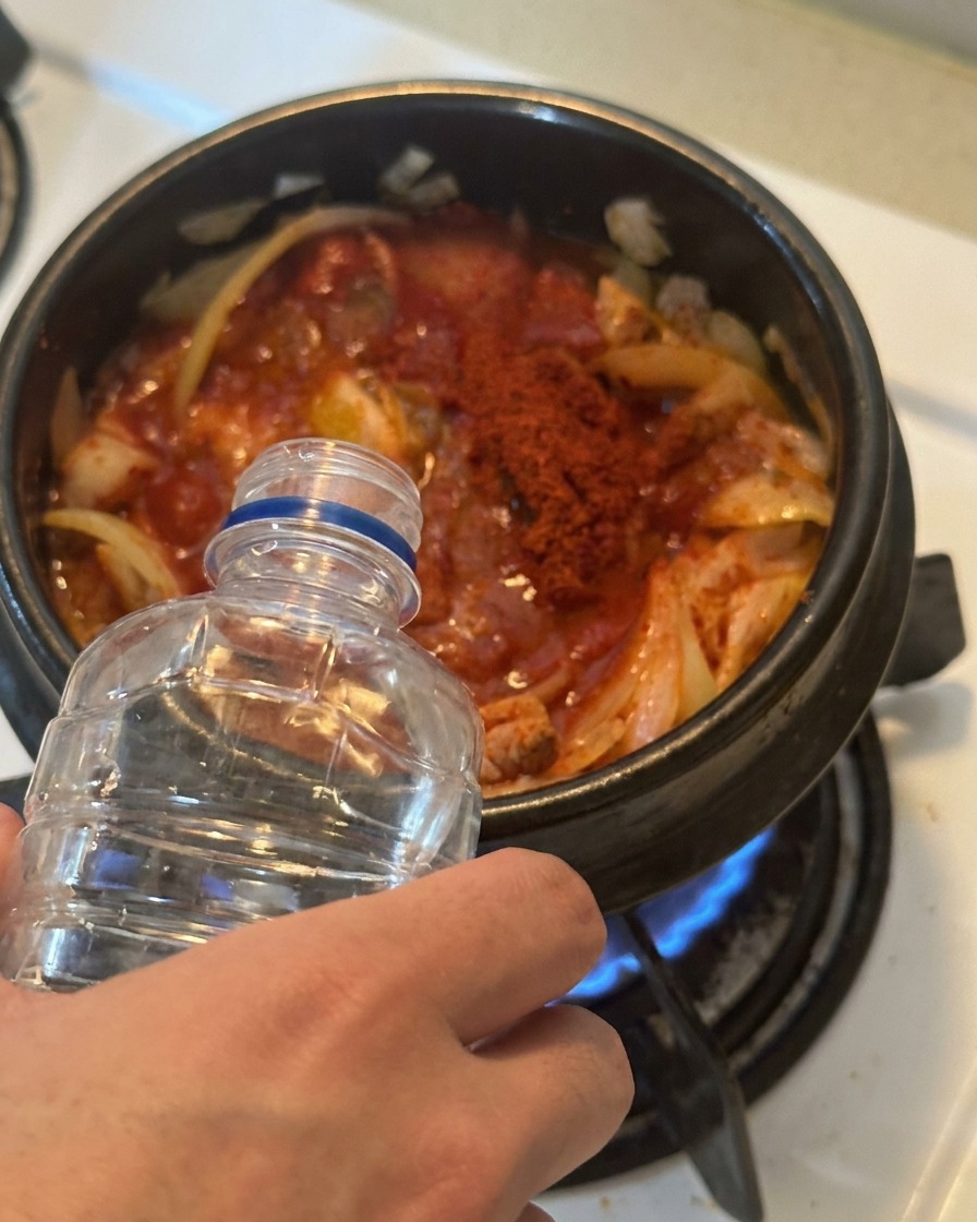 Acqua versata da una bottiglia di plastica trance in una pentola piena di kimchi e tonno conditi di rosso.