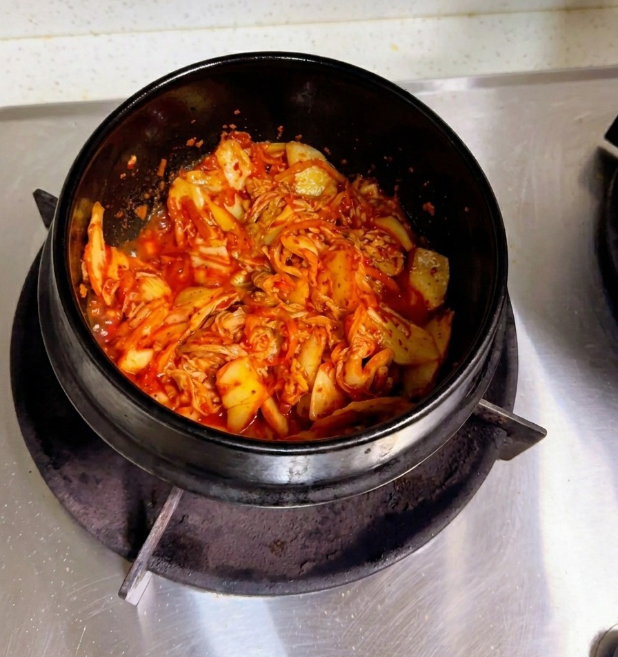 Una mano che versa dellacqua di riso opaca in una pentola di pietra con il kimchi saltato.