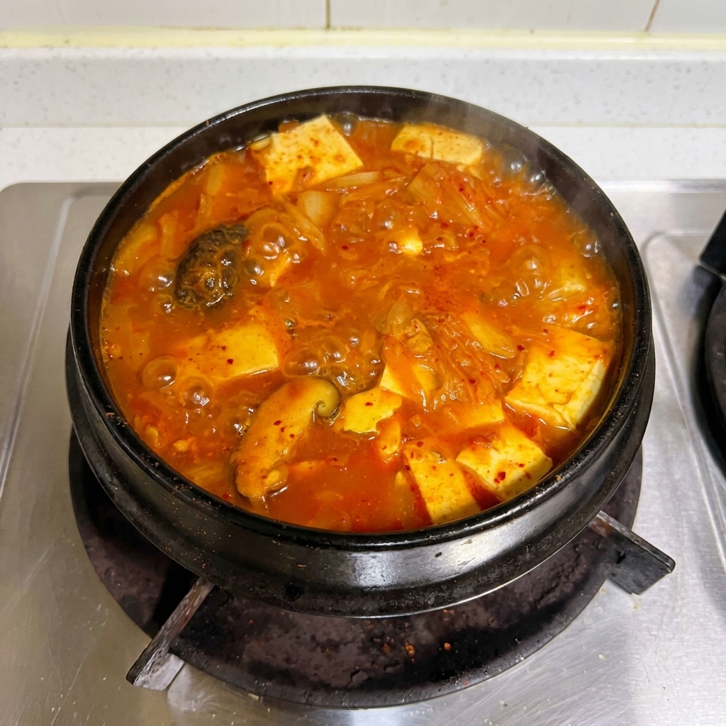 Un vivace stufato rosso di kimchi e tonno che bolle vigorosamente in una tradizionale pentola di pietra sul fuoco.