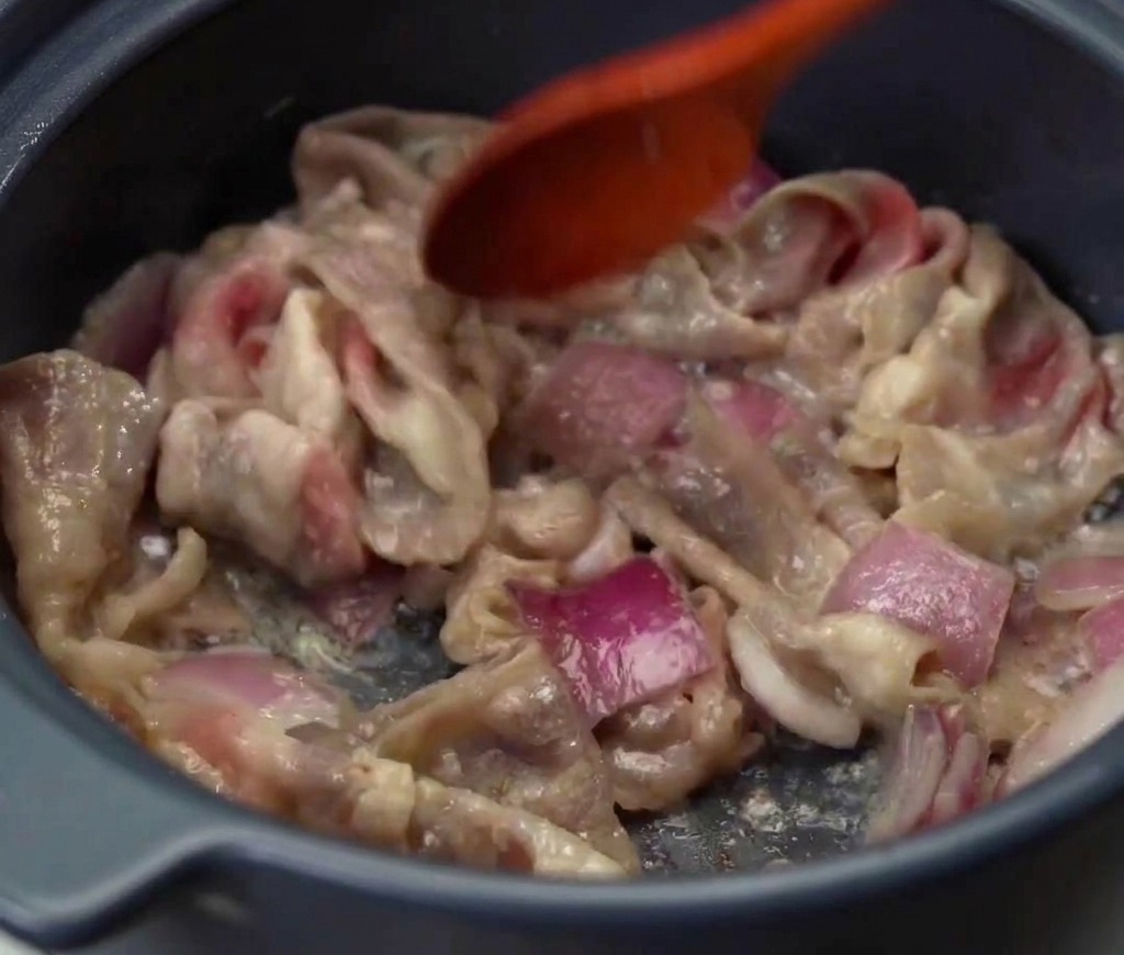 Fettine di manzo e cipolla rossa saltate insieme in una pentola finché la carne non è ben cotta e dorata.