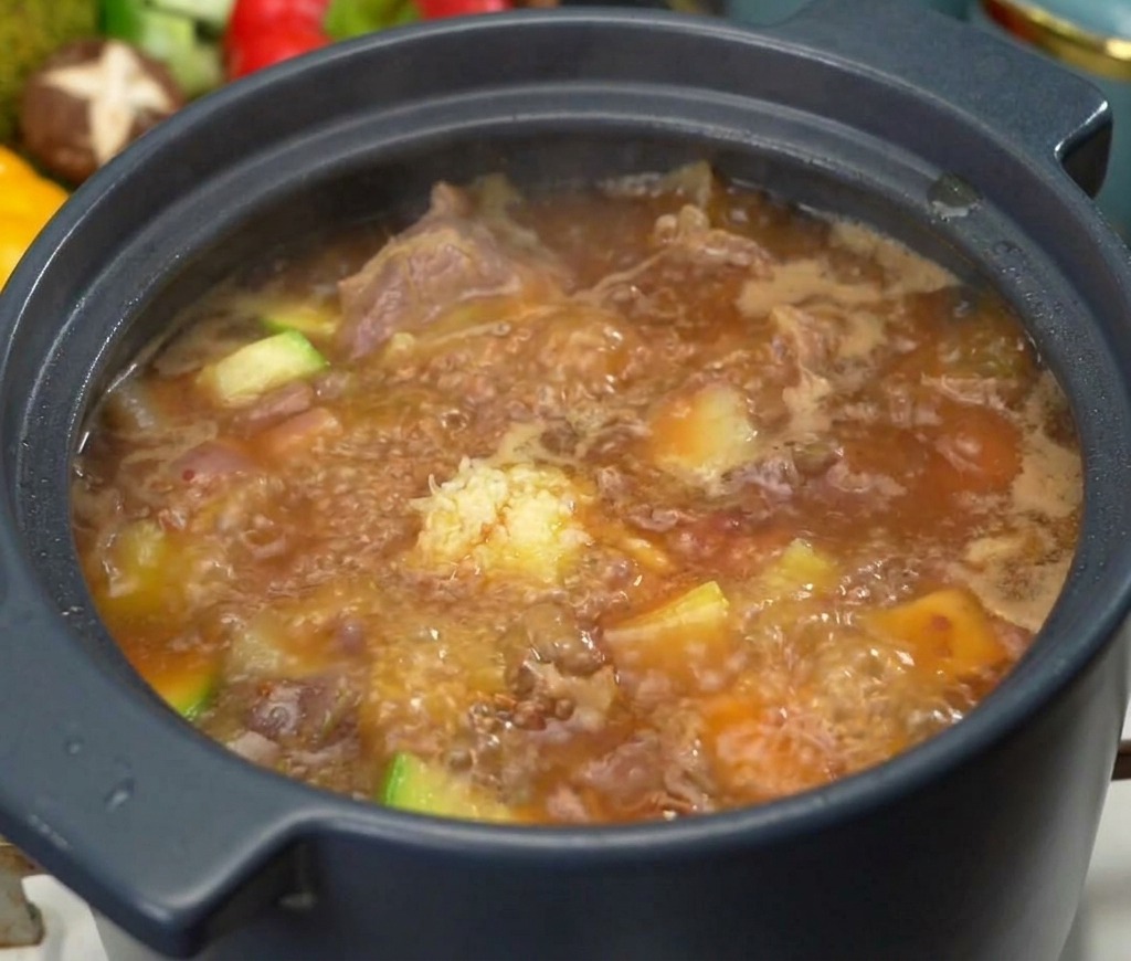 Un cucchiaio di aglio tritato sopra una pentola bollente di zuppa coreana alla pasta di soia con pezzi visibili di carne e zucchine.