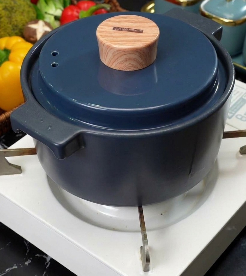 Una pentola in ceramica blu con un elegante coperchio effetto legno posizionata sul bruciatore di un fornello portatile bianco.