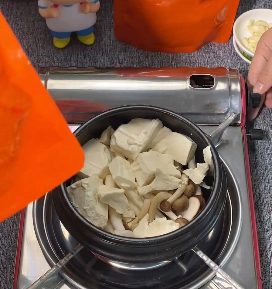 Grandi blocchi di tofu tenero bianco e funghi shimeji disposti in una pentola nera.