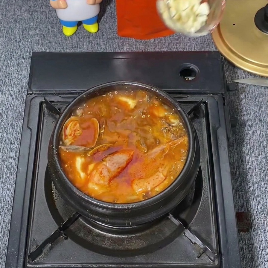 Un mestolo trasparente versa un cucchiaio di aglio bianco tritato al centro di una zuppa coreana piccante e rossa in ebollizione.