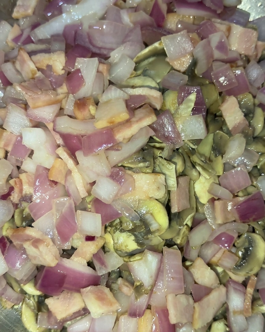 Un mix di funghi dorati saltati, cipolle rosse semitrasparenti e pezzetti di bacon cotti saltati insieme.