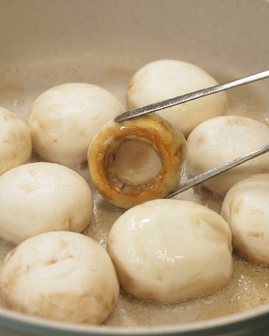 Una pinza gira un fungo in padella mostrando la superficie perfettamente caramellata e dorata della cappella