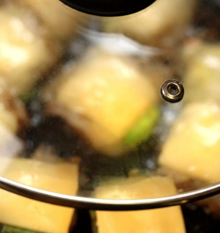 Un coperchio di vetro copre una padella in cui le fette di formaggio iniziano a sciogliersi sopra i burger di funghi