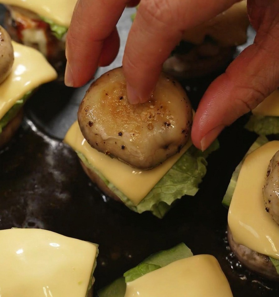 Una mano posiziona una cappella di fungo grigliata sopra un mini burger per completare lassemblaggio nella padella