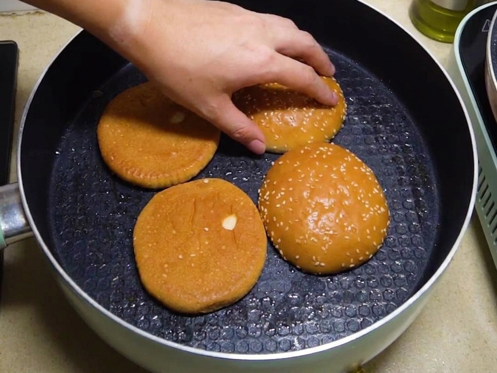 Metà di panini per hamburger tostate a faccia in giù nella padella con il grasso del bacon.